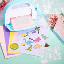 A light blue and white dinosaur craft die-cuting machine shown in use, with colorful dinosaur and jungle-themed paper cutouts displayed on pastel sheets. The scene includes decorative flowers, a pastel desk calendar, and layered paper sheets on a mint green surface.
