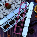 A metal die-cut craft cutting template set displayed on a dark wooden surface with decorative props including a lace doily, acorns, and dried orange slices. The set includes a silver-colored frame template, a dusty rose/pink frame template, and several white paper transfer sheets.