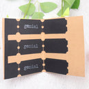 A handmade paper book or journal shown open, featuring three black tabs printed with the word 'genial' in white typewriter font, set against a light textured background with green leaves at the top.