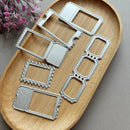 Six silver metal die-cut frames with scalloped and dotted edges arranged on a light wood oval tray, with pink flowers in the top-left corner.