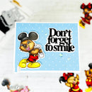 A handmade greeting card featuring a cartoon mouse character in a Mickey Mouse-inspired outfit with the text 'Don't forget to smile' on a light blue polka-dot background. The card is photographed on a white brick-patterned surface with small decorative figurines partially visible around the edges.