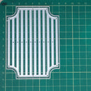 A clear plastic die-cut template or stencil with a decorative border and vertical slotted design, placed on a green cutting mat with grid lines.