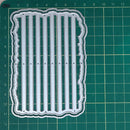 A clear acrylic or plastic embosser or stamping plate with vertical slits and a wavy border, placed on a green cutting mat with measurement markings.