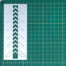 A white rectangular stencil or template sheet with a repeating chevron pattern, placed on a green cutting mat with grid lines.