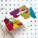 A handmade layered card with colorful geometric tabs in purple, olive green, teal, red, and yellow, decorated with 3D flowers, green leaves, and a small white banner reading 'You're the best dad influence.' The card is photographed on a white peg-hole board with metal dies partially visible at the edges.