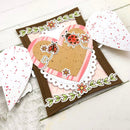 A handmade layered paper heart card with a brown border, pink striped heart, tan center, ladybug and flower details, shown on a white wood background with matching heart cutouts.