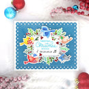 A square handmade Christmas greeting card with a scalloped blue border and colorful bird illustrations, photographed on a white surface with red and blue holiday ornaments around it.