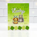 A St. Patrick's Day greeting card featuring a green gradient background with shamrock text, the words 'FEELING Lucky' in white script, a cartoon dog wearing a hat with three shamrocks, a cartoon cat sitting in a pot, and a row of die-cut shamrocks along the bottom edge.