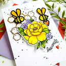 A handmade greeting card featuring a large yellow rose, two bees, purple flowers, and the word 'be well' in black script, styled with colorful envelopes and green leaves.