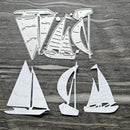Three white metal nail art dies shaped like sailboats, displayed on a dark gray wood-grain background.