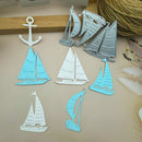 Six paper cutout sailboat and anchor shapes in light blue and white, arranged on a beige surface with a wooden strip and rope in the background.