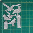 A set of six metal bird-shaped craft dies displayed on a green cutting mat with grid lines and centimeter measurements.