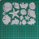 A set of 15 plastic craft dies shaped like seashells, starfish, and coral, displayed on a green cutting mat with grid lines.