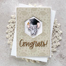 A handmade graduation card featuring a cute cartoon elephant wearing a black graduation cap, with the word 'Congrats!' in metallic gold script. The card is layered over a white card and styled on a textured gray surface with a cream lace doily.