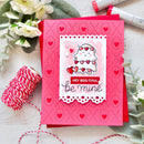 A handmade Valentine's Day greeting card with a pink perforated border, a white central panel featuring a cute cartoon character with hearts, and the text 'HEY BOO-TIFUL be mine'. The card is styled on a white surface with red-and-white bakers twine, white flowers, green leaves, and craft markers.