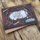 A handmade layered cardboard greeting card with a dark brown and black scalloped frame, featuring a cartoon dog with a broken tooth and white bones, resting on a kraft envelope over a rustic wood background.