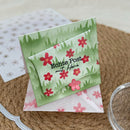 A handmade German postcard with a green watercolor grass background and red flowers, featuring the text 'Echte Post mit Herz'. It is displayed on top of a matching patterned envelope on a woven straw mat.