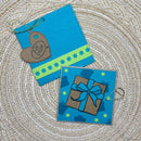 Two handmade blue greeting cards or tags laid flat on a woven beige surface. One card has a brown heart-shaped tag with a string loop and the words 'for you', and the other features a brown gift box with a blue ribbon and bow illustration.