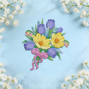 A colorful embroidered floral patch depicting yellow crocuses, purple tulips, green leaves, and a pink ribbon, displayed on a light blue marble background with white baby's breath flowers framing the edges.