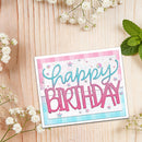 A handmade 'Happy Birthday' greeting card styled on a light wood background with white baby's breath flowers and mint leaves. The card features a white base with pink and light blue plaid borders, a white glittery center, and raised pink and blue lettering.