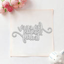 A silver metal die-cut lettering template featuring the phrase 'I love you silently' in elegant cursive, displayed on a square sheet of white cardstock. The setup is styled as a flat-lay with pink roses in the top-left corner and a small white ceramic pig in the bottom-right corner, all on a clean white background.