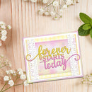 A handmade greeting card with the phrase 'forever STARTS today' in gold and pink script, layered over pastel pink, yellow, and white textured paper. The card is styled on a light wood background with white baby's breath flowers and mint leaves.