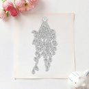 A silver metal floral hanging ornament die-cut template or craft cutout shown on a square sheet of white cardstock, styled with pink flowers in the top-left and a small white ceramic object in the bottom-right on a light background.