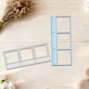 Two metal photo frame templates, one silver and one light blue, displayed on a light wood background with dried flowers and white blossoms.