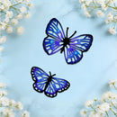 Two butterfly-shaped decorative wall art pieces with blue and purple marbled wings and black outlines, displayed on a light blue marble surface with white baby's breath flowers in the corners.