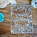 A laser-cut metal birthday card or plaque with 'Happy Birthday' script, bunting, stars, and gift boxes, displayed on a wooden surface with decorative flowers and a candle nearby.