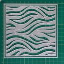 A square clear acrylic cutting mat with an intricate wavy pattern, displayed on a green gridded cutting mat. The mat features a double border and is shown from a top-down perspective.