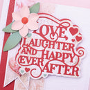 A decorative handmade card featuring the phrase “LOVE LAUGHTER AND HAPPY EVER AFTER” in red script, layered over a white and pink patterned background. A pale pink flower with green leaves and small red hearts decorate the upper left area.