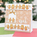 A handmade Christmas greeting card with gingerbread-themed decorations, including gingerbread people, houses, trees, and the word 'Noel' in white script, displayed on a table with a blurred festive background.