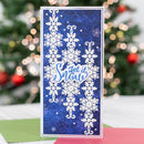 A handmade greeting card with a blue textured background, white layered snowflakes, and the phrase 'Let it Snow' in blue script, displayed in front of a blurred Christmas tree with lights.