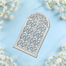 An arched metal die-cut template with an intricate geometric and scrollwork pattern, displayed on a light blue marble background with white baby's breath flowers in the corners.