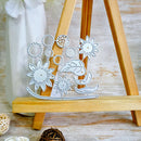 A set of white metal laser-cut dies featuring floral, leaf, and bird motifs, displayed on a small wooden A-frame easel.