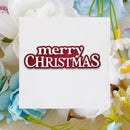 A square white card with torn paper edges featuring the words 'merry CHRISTMAS' in red and white lettering, surrounded by artificial white, blue, and yellow flowers on a beige fabric background.