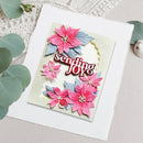A handmade greeting card with pink poinsettia flowers, blue leaves, and the words 'sending JOY' in raised lettering, styled on a white textured cardstock with eucalyptus leaves around it.