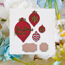 A white square card with Christmas ornament-shaped embellishments and two blank blush pink pieces, styled among white and blue flowers on a beige fabric background.