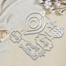 A flat-lay of a metal die-cutting or crafting template set featuring Christmas-themed shapes, including ornaments, stars, and cursive text, arranged on a textured cream fabric with cotton stems.