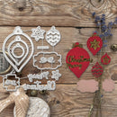A flat-lay of Christmas-themed crafting tools and embellishments on a rustic wooden background, including a silver metal die set and red decorative ornaments with gold glitter accents.