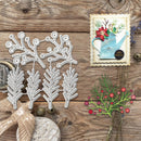 A flat-lay of a white metal die-cutting or crafting template featuring holly and berry branches, displayed on a rustic wooden surface alongside decorative craft props and a handmade card.