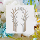 A square white card with two sets of bare tree branches in light beige and brown tones, styled on a burlap surface with white and blue flowers around it.