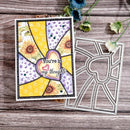 A handmade greeting card with a patchwork sunflower design and the phrase 'You're in my thoughts' is displayed next to a metal die-cutting or stamping template on a rustic wooden surface with small flowers.