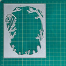 A silver metal die-cutting template with a coral reef and sea life silhouette design, displayed on a green cutting mat with measurement markings.
