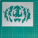 A metal cutting die with a spooky jack-o'-lantern face and tree silhouette cutout, displayed on a green cutting mat with grid lines.