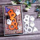 A Halloween-themed card with layered orange 'BOO' lettering, white ghost cutouts, black spiderwebs, and a purple witch hat on a brick-patterned background, displayed beside matching white ghost and witch hat die-cut pieces on a wood surface with flowers.