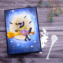 A handmade Halloween-themed card featuring a witch riding a broomstick in front of a full moon, displayed on a rustic wooden surface alongside die-cut decorative elements.