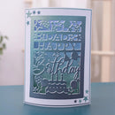 A handmade layered paper card with a laser-cut 'Happy Birthday' design, featuring stars, balloons, and a birthday cake, displayed on a blue surface with a blurred indoor background.