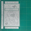 A silver metal stamping or embossing plate with decorative cutout lettering and hearts, shown on a green gridded cutting mat.